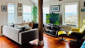 Un salon comprenant un canapé, un fauteuil jaune, un téléviseur et une structure en poutres apparentes.