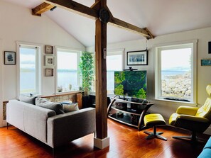 A living room with a sofa, a yellow chair, a TV, and a wooden beam structure. - Beachfront Cottage on Beautiful St Margarets Bay - Ingramport, Nova Scotia (Ingramport)