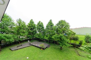 A grassy outdoor area with a wooden deck, benches, and potted plants.