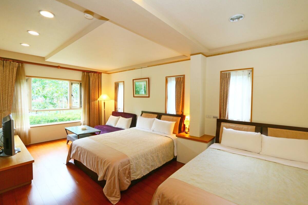 A hotel room with two beds, a desk, a TV, and a window with curtains.