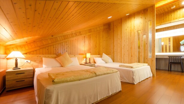 Una habitación con paneles de madera, dos camas, mesitas de noche y un banco.