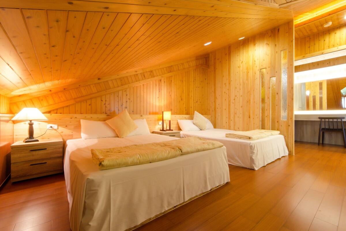 A wooden-paneled room with two beds, nightstands, and a bench.