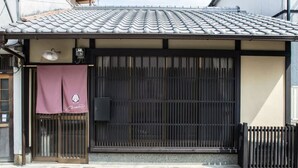 A traditional Japanese building with a tiled roof, a sliding door, and a small awning with a logo. - Kyo Cottage Machico Mibu (Kyoto)