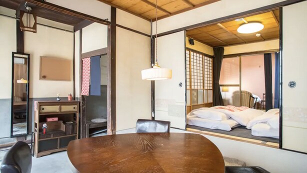 A traditional Japanese-style room with tatami flooring, a wooden table, a low wooden cabinet, and a sliding shoji screen door. - Kyo Cottage Machico Mibu (Kyoto)