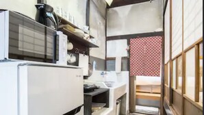 A narrow kitchen with a white refrigerator, a sink, and a small window. - Kyo Cottage Machico Mibu (Kyoto)