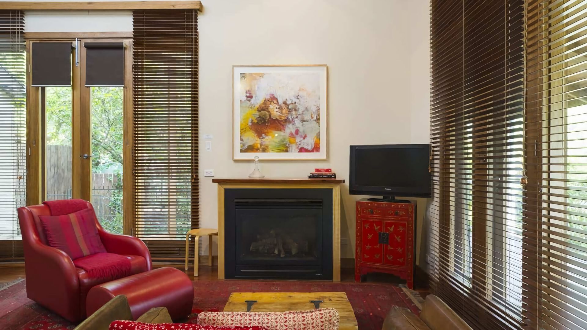 A living room with a red leather chair, a fireplace, a flat-screen TV, and a painting on the wall.