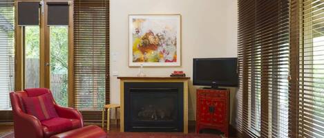A living room with a red leather chair, a fireplace, a flat-screen TV, and a painting on the wall.