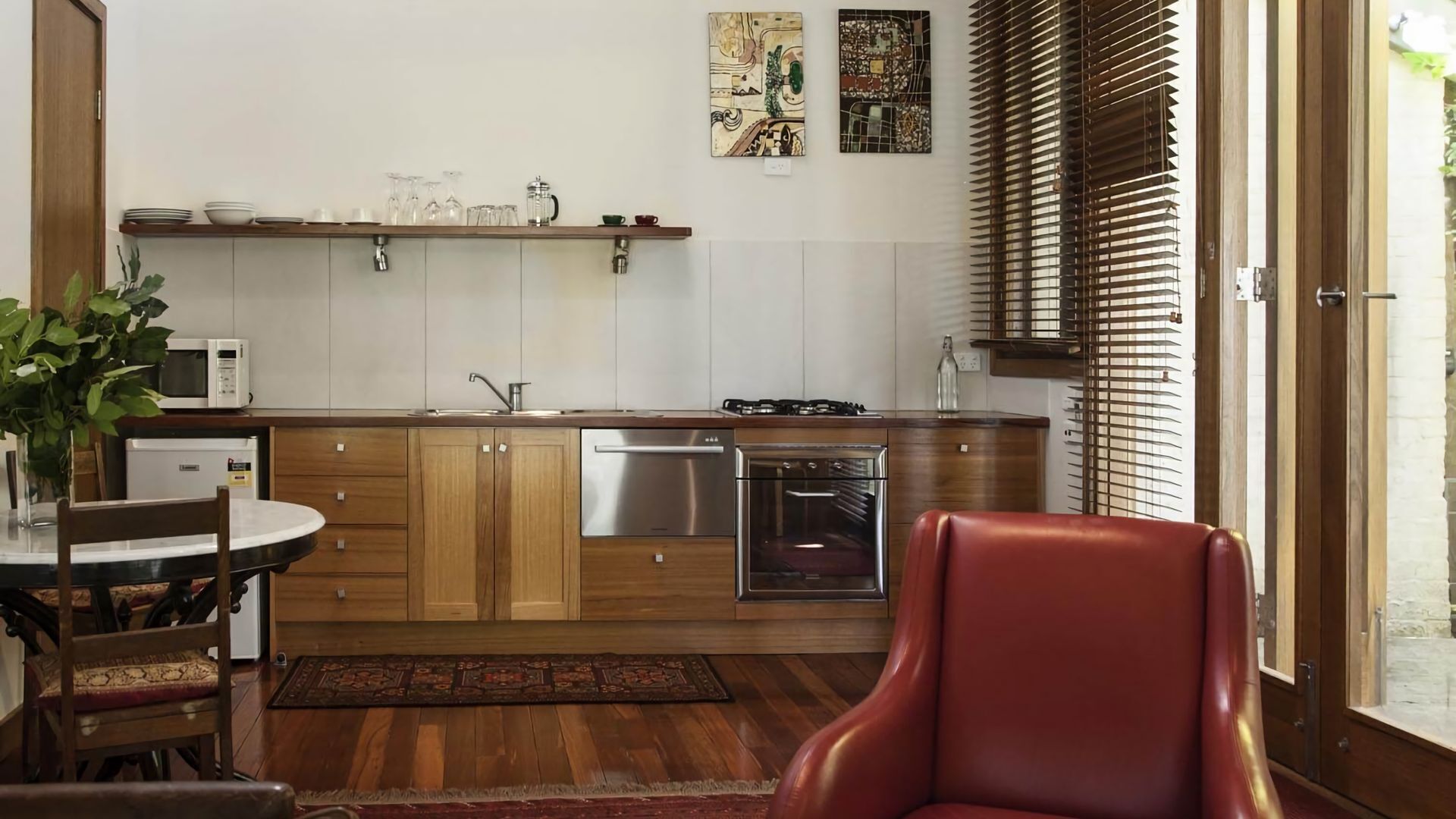 A modern kitchen with wooden cabinets, stainless steel appliances, and a dining area with a red chair.