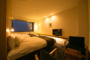 A hotel room with a bed, a desk, a chair, a TV, and a window. - The Guernsey Hotel & Resort (Taketa)
