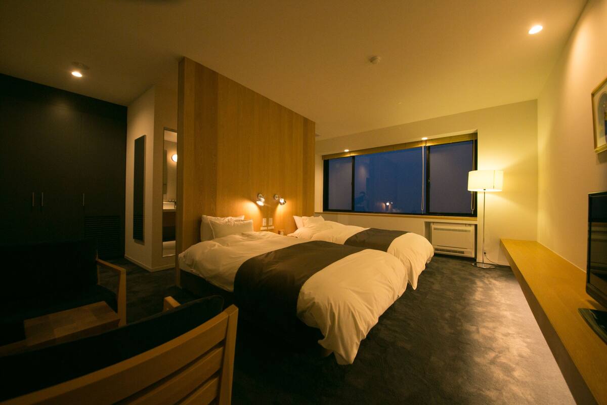 Une chambre d’hôtel moderne avec deux lits, un bureau et une grande fenêtre.