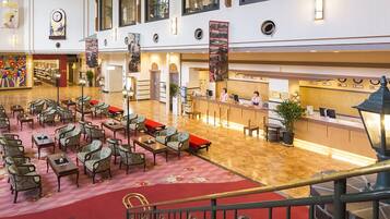 A hotel lobby with multiple seating areas, a reception desk, and a staircase.