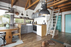 A kitchen with wooden beams, a dining table, chairs, a ladder, and a view of the outdoors.
