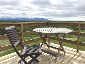 A wooden deck with a table and a chair, overlooking a mountainous landscape.