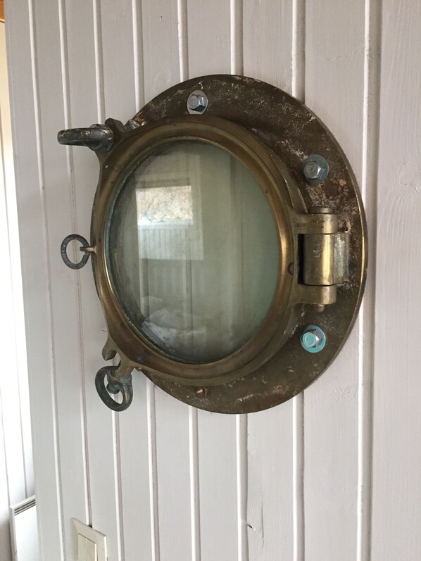 A porthole window with a brass frame and glass, mounted on a white paneled wall.