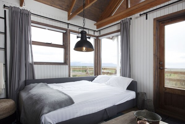 A bedroom with a large bed, a hanging light fixture, and a view of the outdoors.