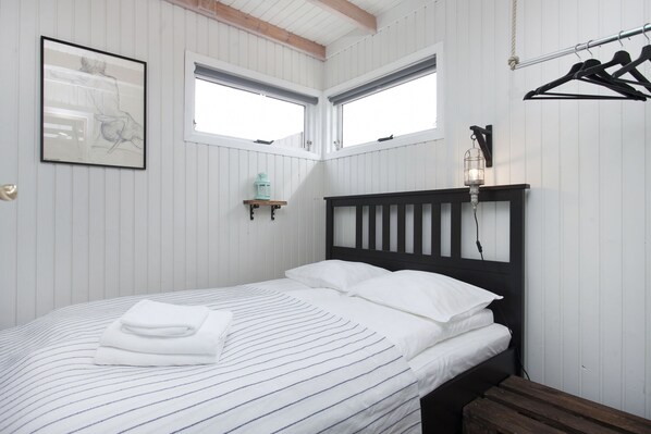 Una cama bien tendida con ropa de cama a rayas, un cabecero negro y una pequeña estantería con un farol.