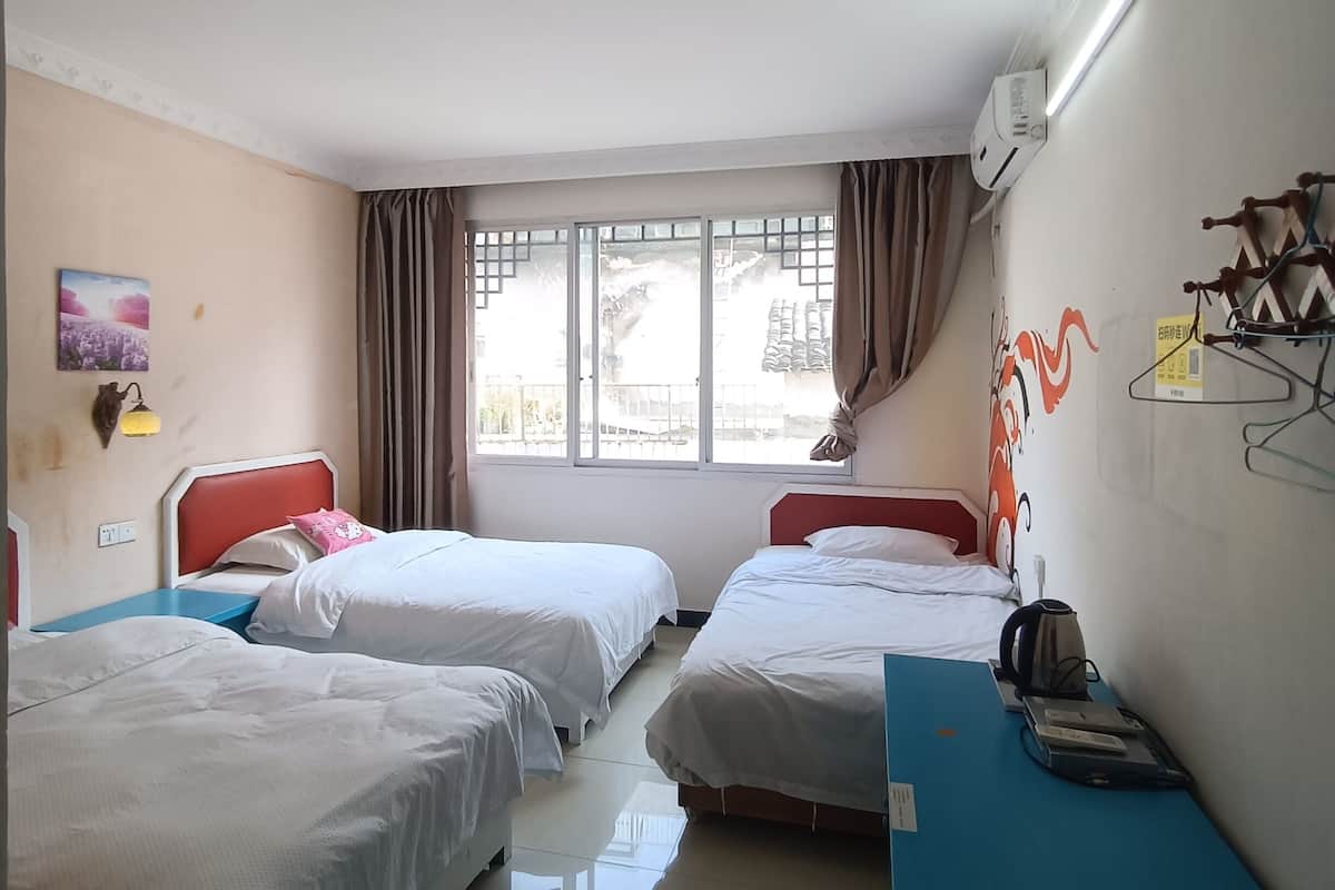 A hotel room with two beds, a desk, a chair, a window with curtains, and a wall-mounted air conditioner.