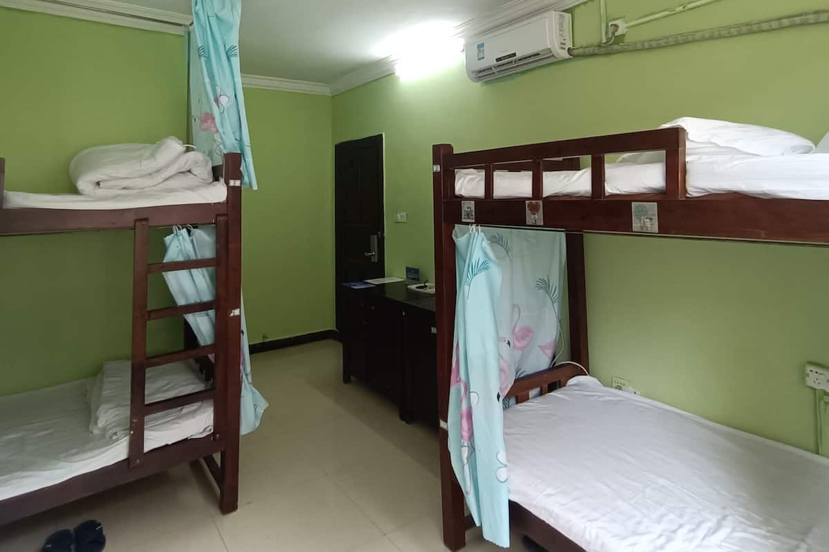 A dormitory room with bunk beds, a desk, and an air conditioning unit.