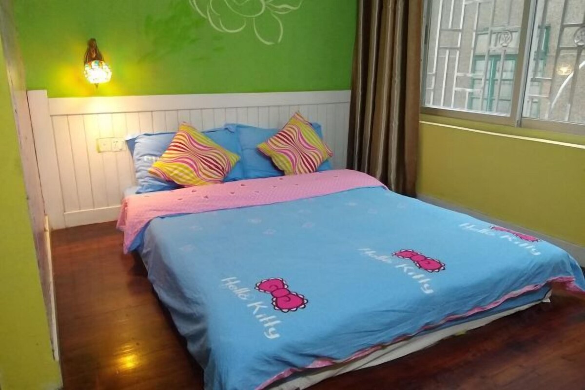 Una habitación con una cama, una lámpara en la pared y un ventanal con cortinas.