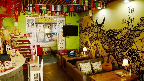 A cozy room with a green wall, a wooden table, a sofa, and a guitar. - How Flower Hostel Yangshuo (Guilin)