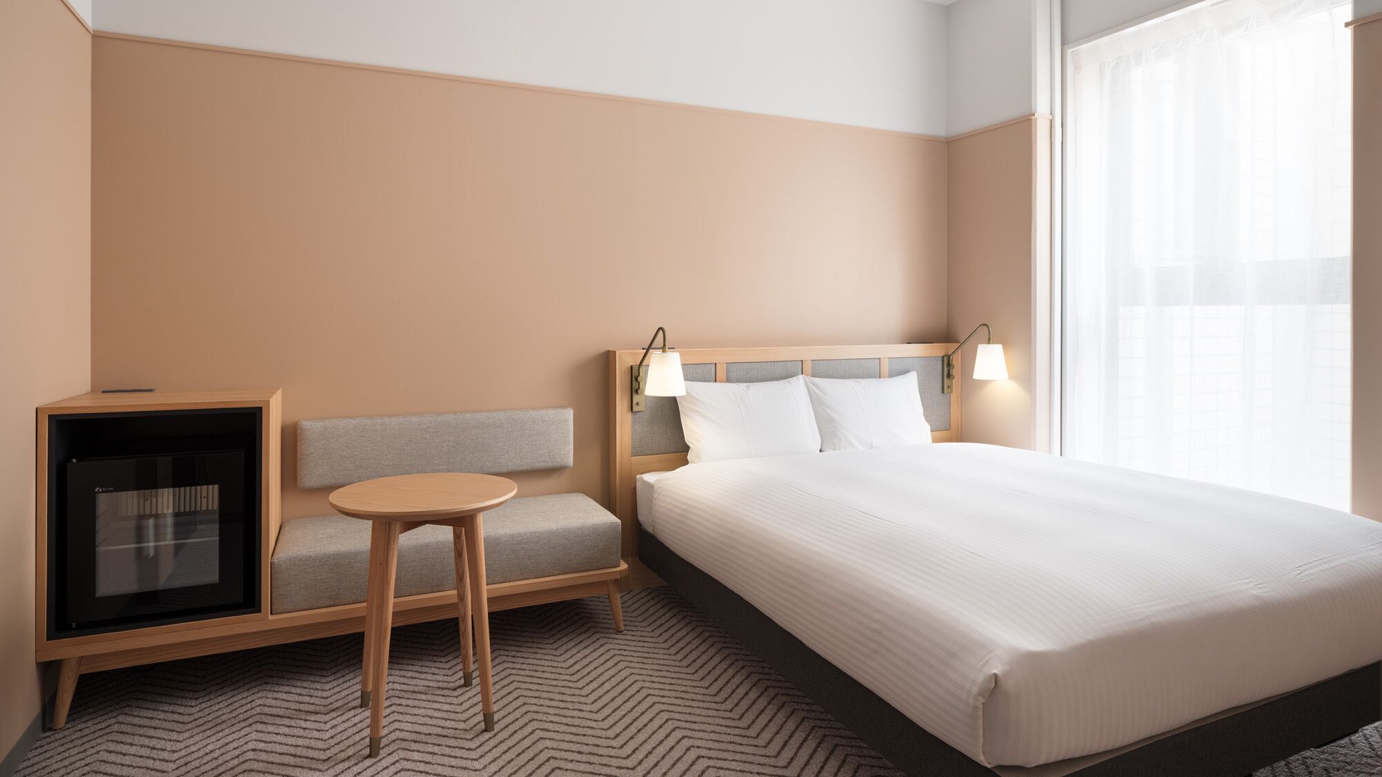 A hotel room with a bed, a seating area with a table, a TV, and a window with curtains.