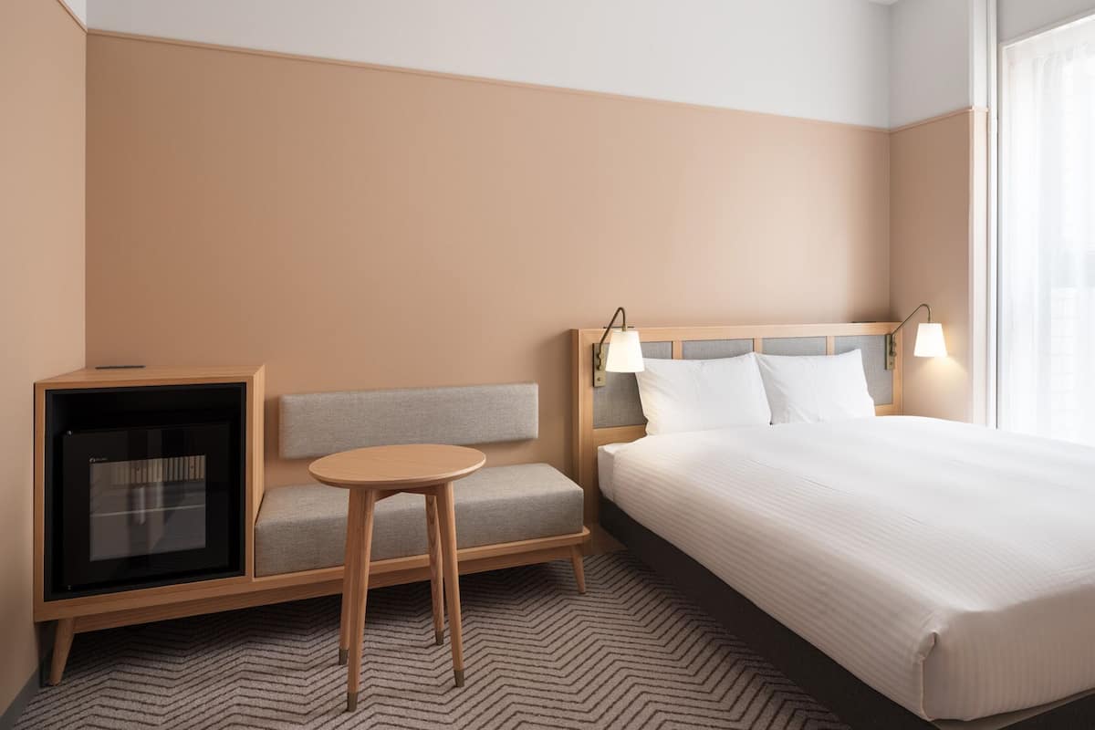A hotel room with a bed, a seating area with a table, a TV, and a window with curtains.