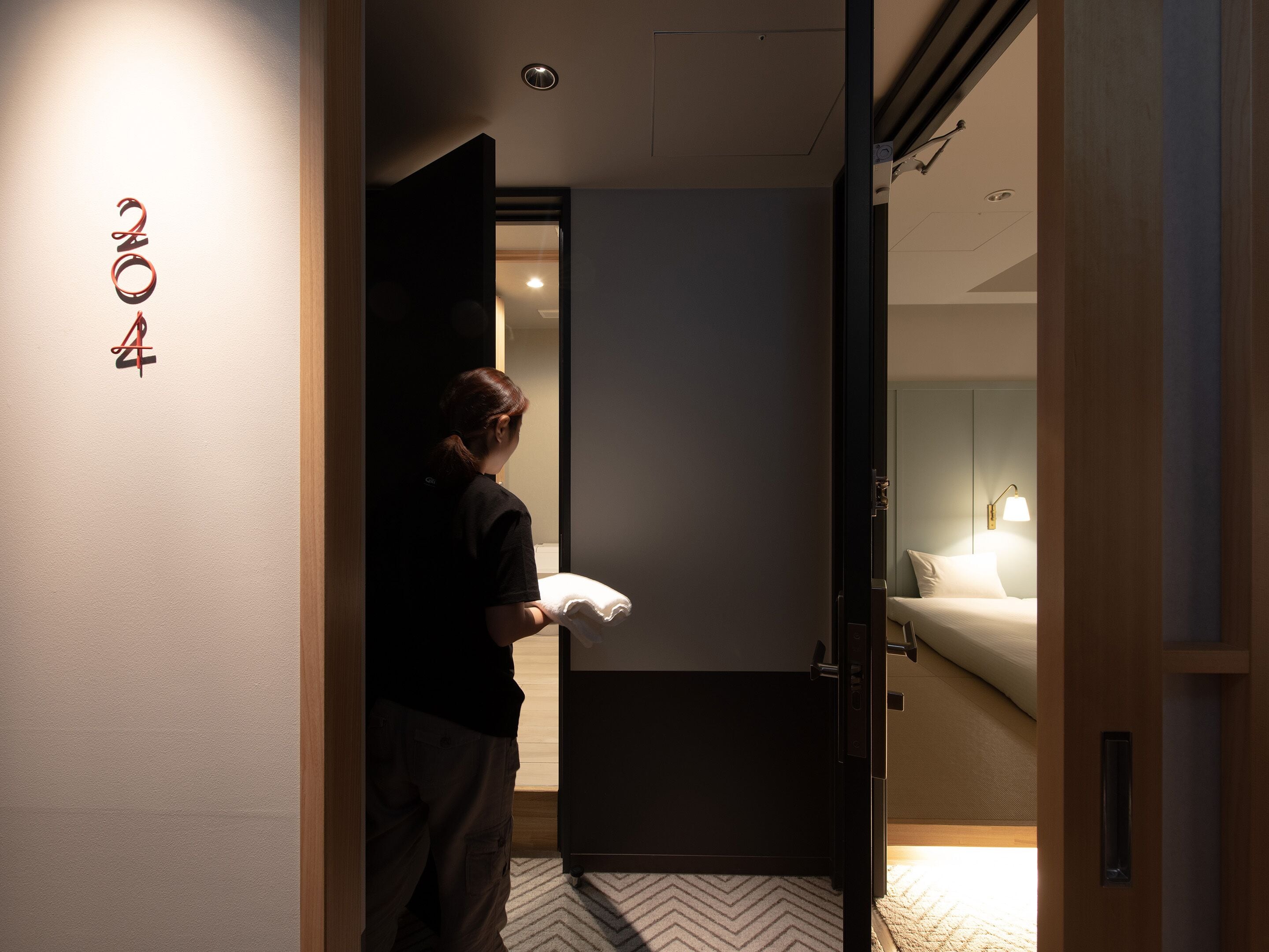 A hotel room with a bed, a nightstand, and a door leading to another room.