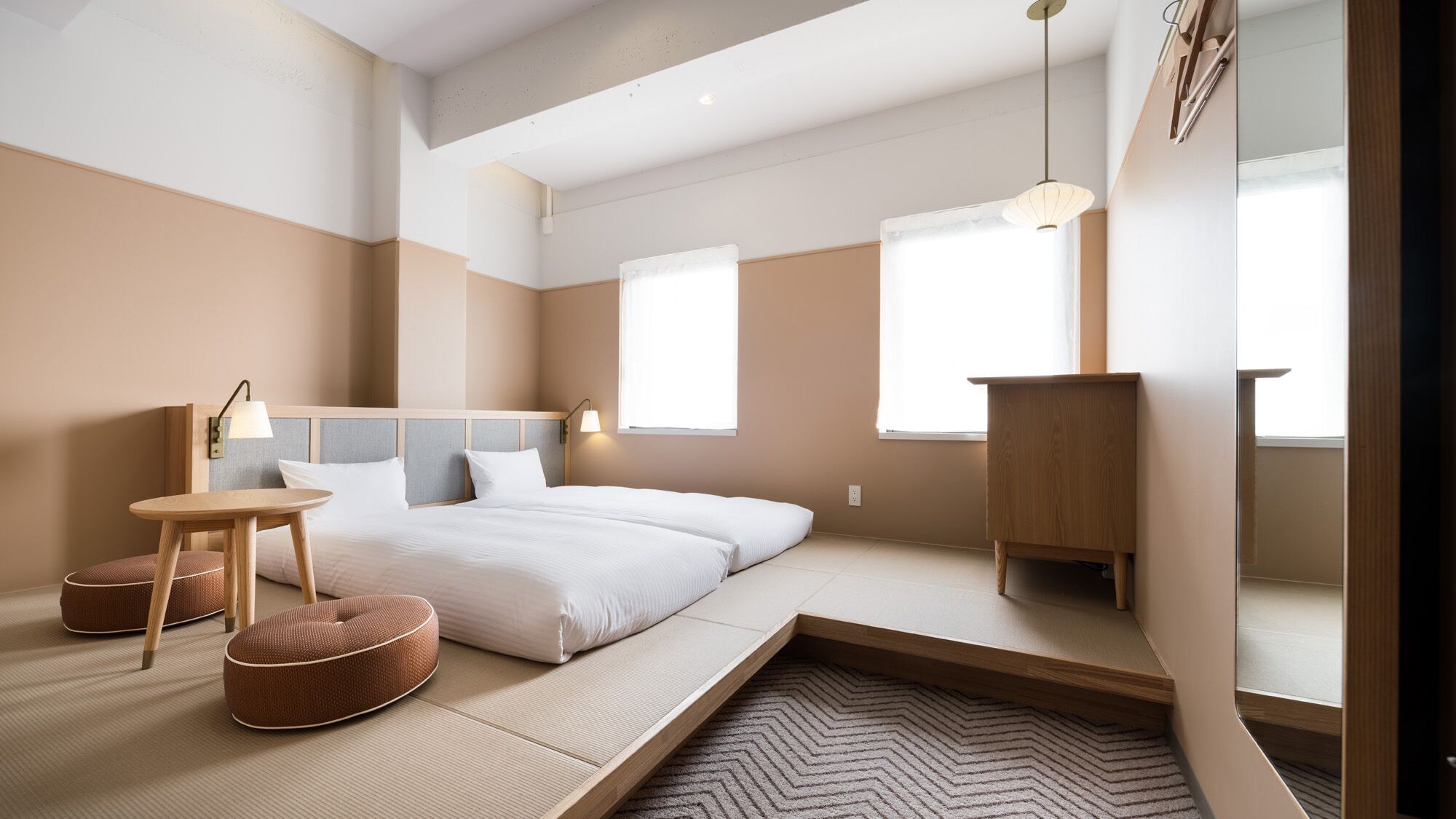 Quarto moderno com cama, mesas de cabeceira, uma mesinha e um espelho.