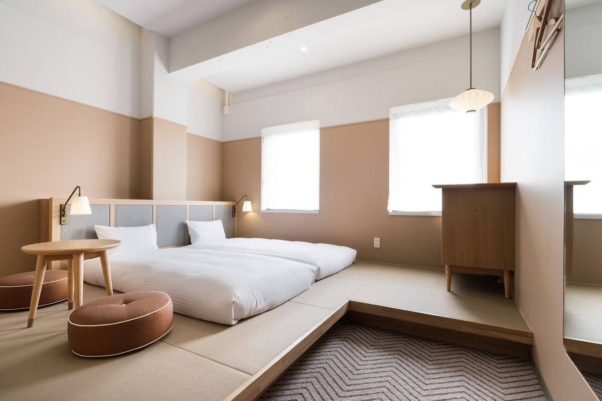 A modern bedroom with a bed, bedside tables, a small table, and a mirror.