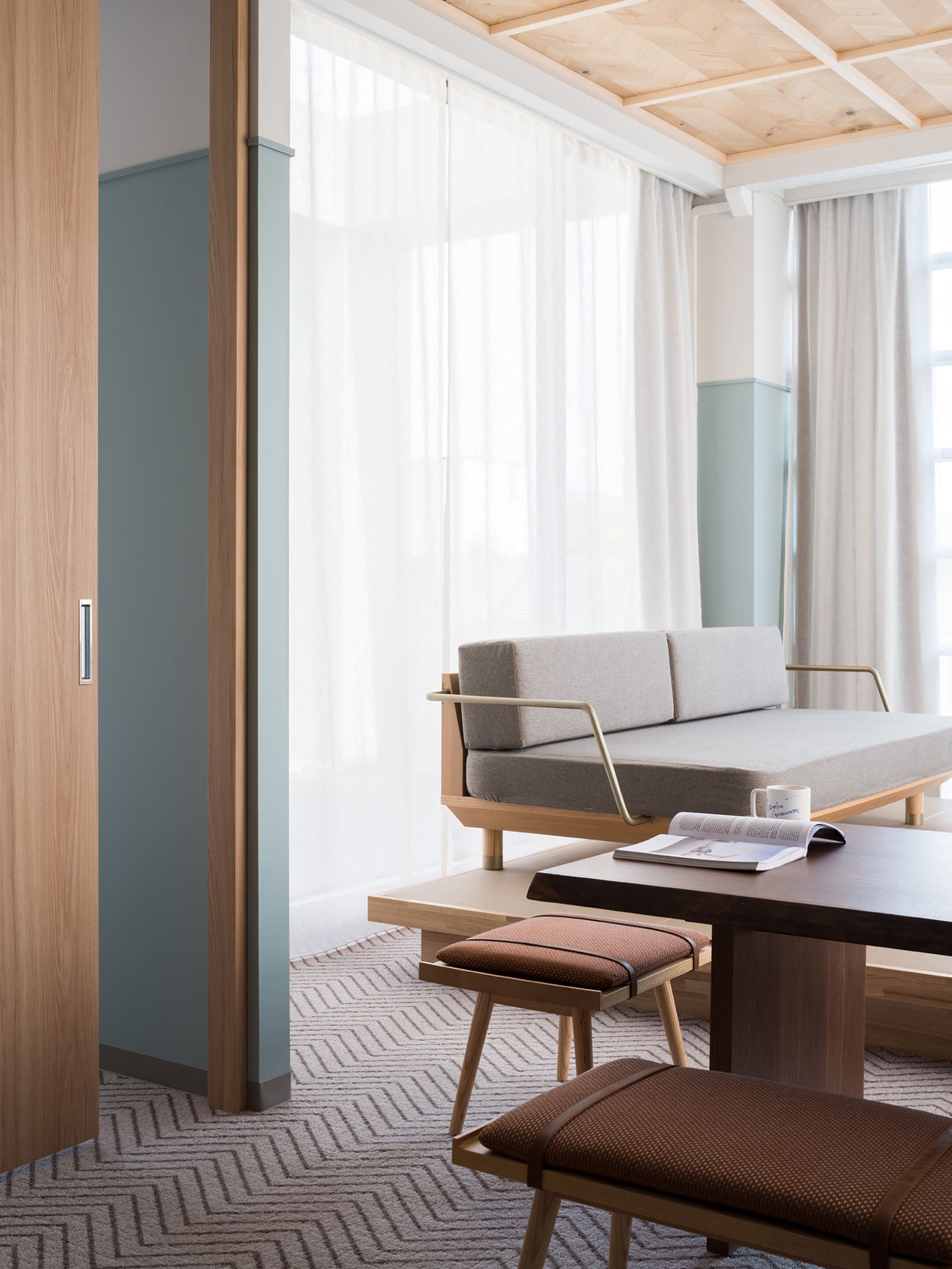 A modern hotel room with a wooden ceiling, a sofa, a table, and a chair.