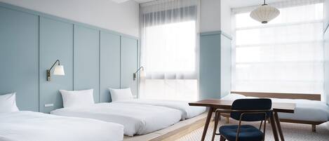 Habitación de hotel con dos camas individuales, un escritorio de madera, una silla y un ventanal con cortinas de gasa.