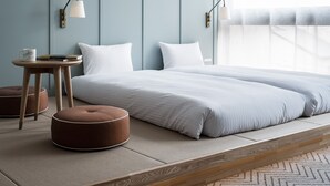 A modern bedroom with a large bed, two bedside tables, a small round ottoman, and a nightstand with a lamp. -  RAKURO Kyoto by THE SHARE HOTELS (Kyoto)