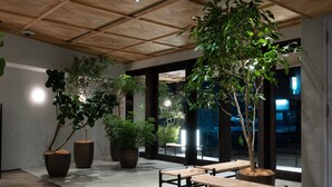 A modern indoor space with wooden ceiling panels, large potted plants, and seating areas. -  RAKURO Kyoto by THE SHARE HOTELS (Kyoto)