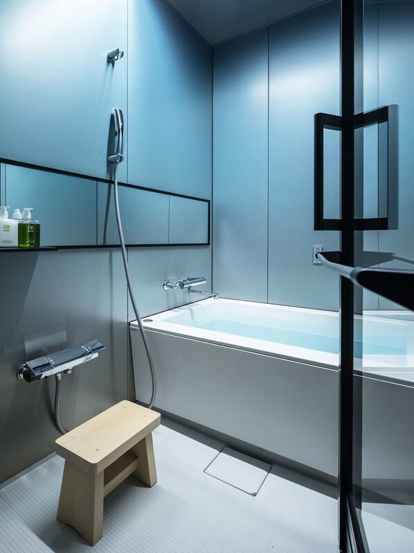 A modern bathroom with a bathtub, a small wooden stool, a glass shower enclosure, and a shelf with toiletries.