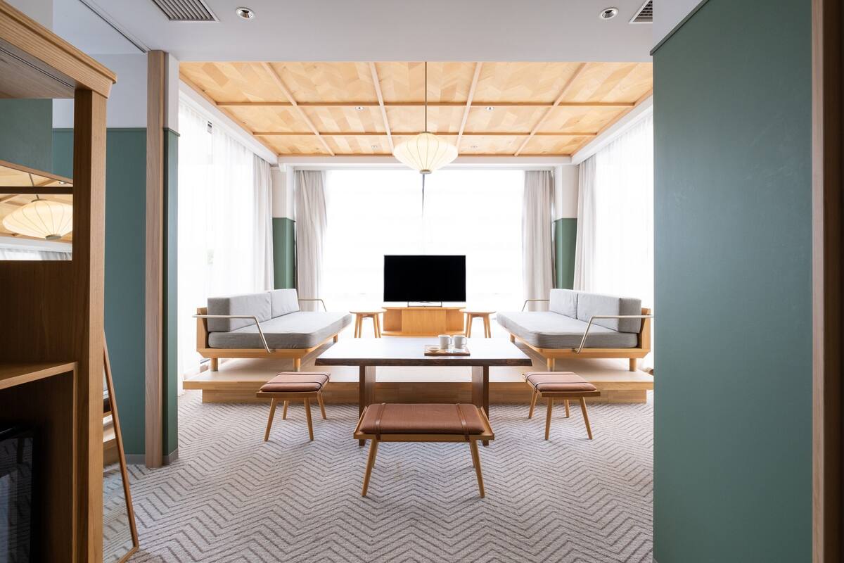 A modern living room with a wooden ceiling, a large TV, two sofas, a coffee table, and a bench.