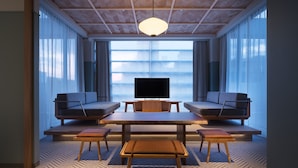 A modern living room with a large flat-screen TV, two sofas, a wooden coffee table, and a bench. -  RAKURO Kyoto by THE SHARE HOTELS (Kyoto)