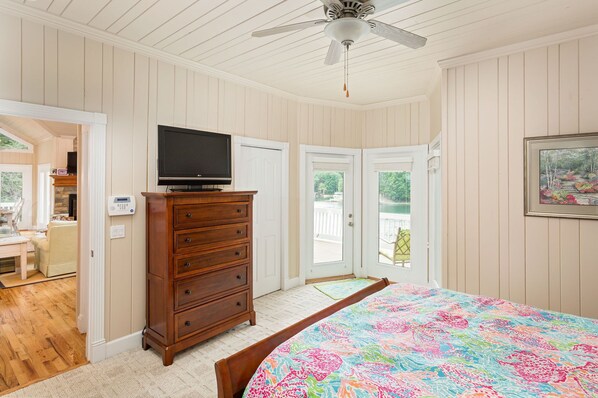 A bedroom with a bed, dresser, TV, and a view of a lake through a door.