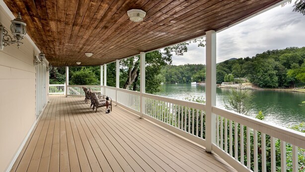 Um deck de madeira com guarda-corpos brancos, com vista para um lago, cercado por árvores.