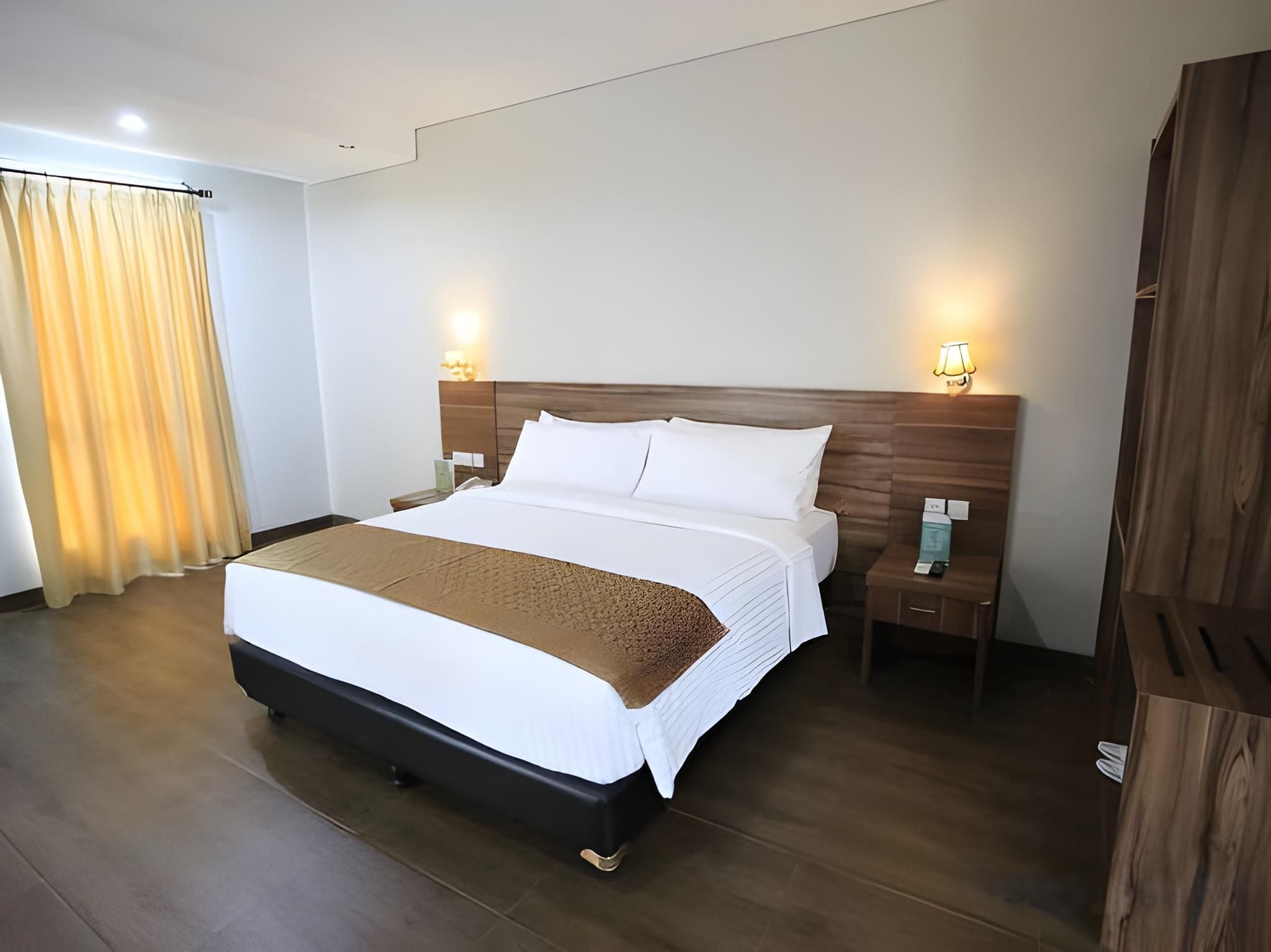 A hotel room with a large bed, wooden headboard, bedside lamps, a nightstand, and a wooden wardrobe.