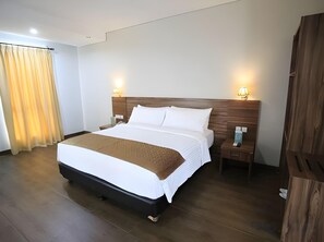 A hotel room with a large bed, wooden headboard, bedside lamps, a nightstand, and a wooden wardrobe. - Azza Hotel Palembang by Horison (Palembang)