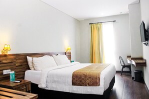 Quarto de hotel com cama, abajures, escrivaninha, cadeira e televisão.