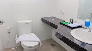 A bathroom with a toilet, sink, and mirror. - Azza Hotel Palembang by Horison (Palembang)