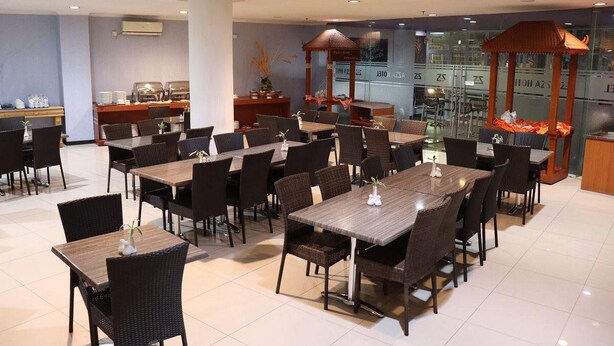 A hotel dining area with multiple tables and chairs, a kitchen in the background, and a decorative gazebo. - Azza Hotel Palembang by Horison (Palembang)