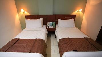 A hotel room with two single beds, a nightstand with a phone and books, and wall-mounted lamps.
