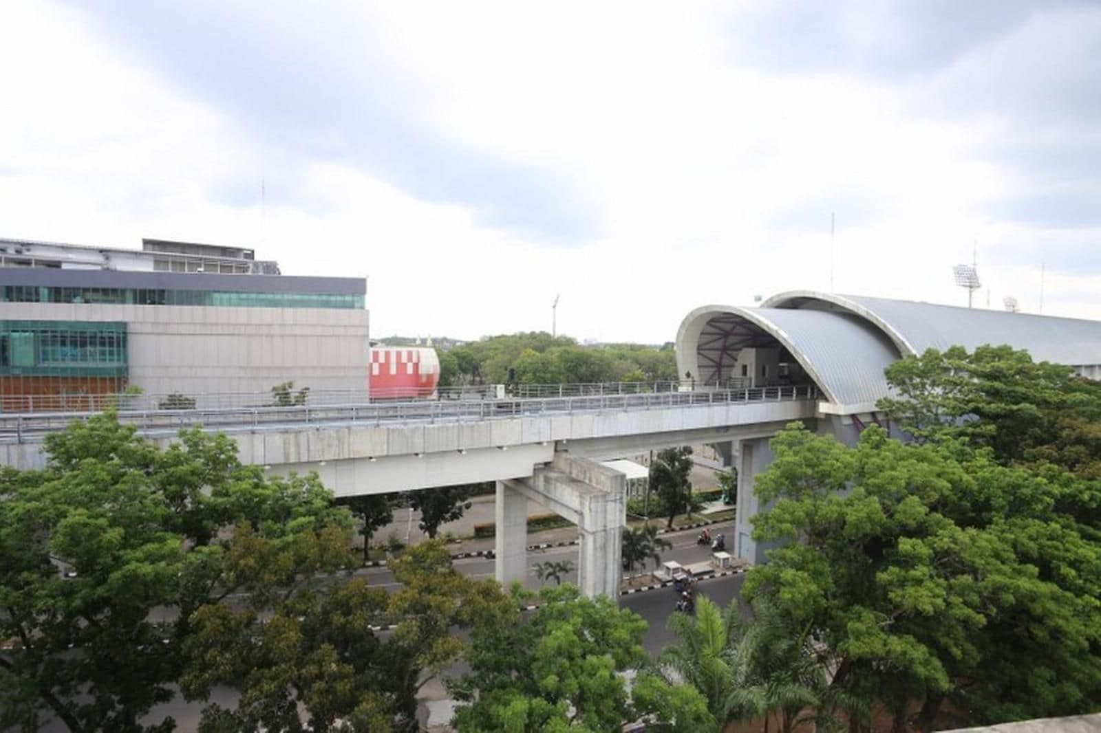 A bridge with a tram passing over it, a modern building with a curved roof, and trees in the foreground.