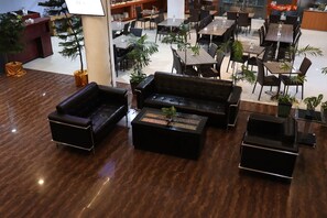 Amplo espaço interno com diversas mesas e cadeiras para refeições, um balcão de recepção e vários vasos de plantas.