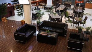 A spacious indoor area with multiple dining tables and chairs, a reception desk, and several potted plants. - Azza Hotel Palembang by Horison (Palembang)