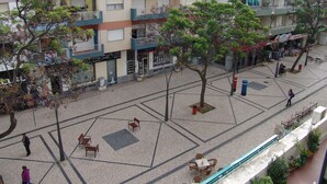 Ein Platz mit Fliesenboden, Bänken und Kübelpflanzen.