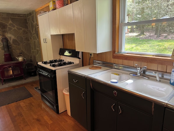 A compact kitchen with a stove, sink, and wooden cabinets. - Cozy cabin nestled the woods (Warriors mark)