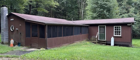 A two-story wooden building with a brown exterior, a covered porch, and a small attached shed.